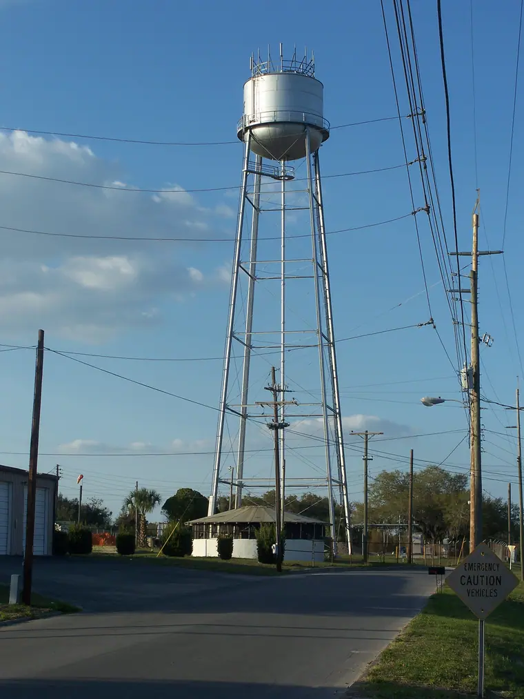 A tall silver water tower lettered FROSTPROOF standing above trees against a clear sky.