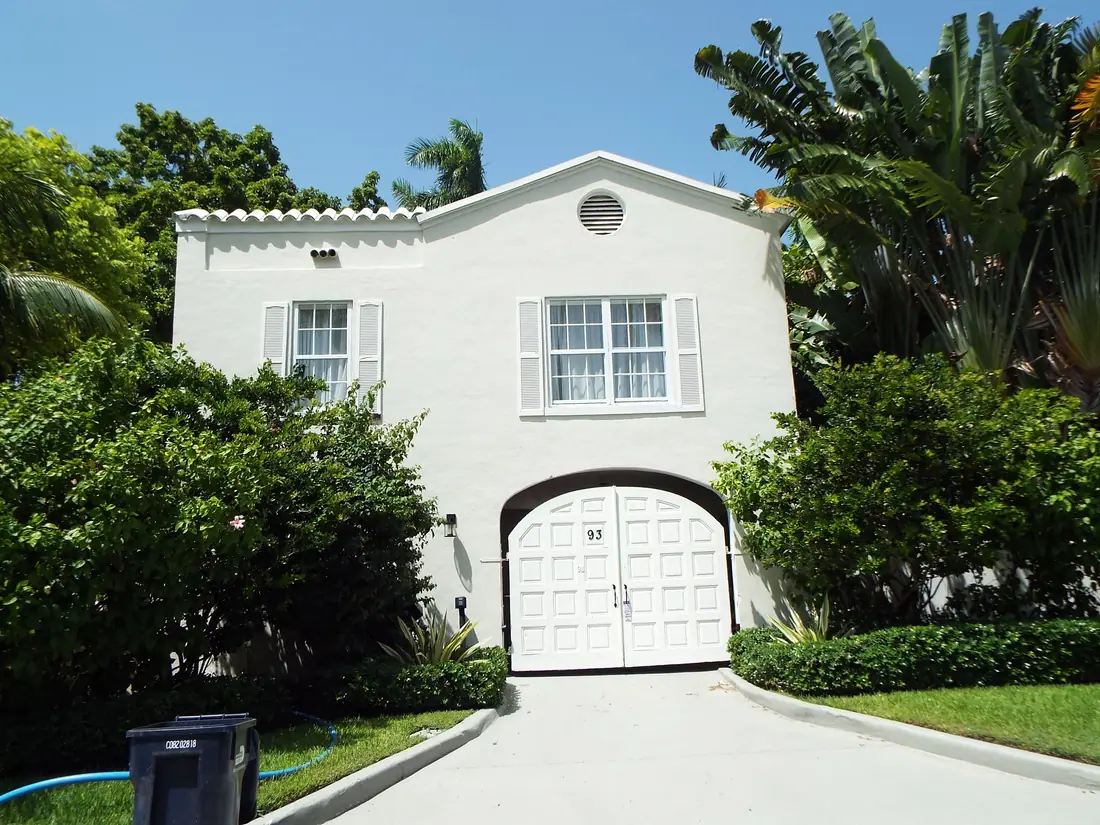 Gated entrance to a walled waterfront estate on Palm Island, Miami Beach, with palms and a driveway beyond.