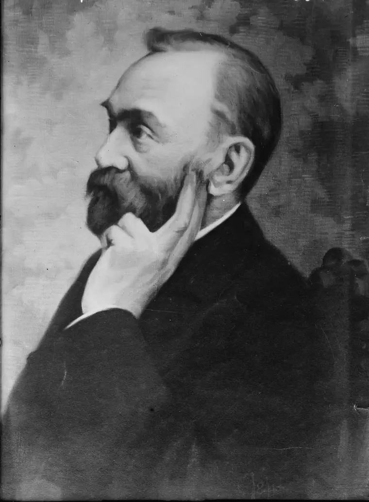 Studio photograph of Alfred Nobel, bearded and in a dark coat, seated in three-quarter view.