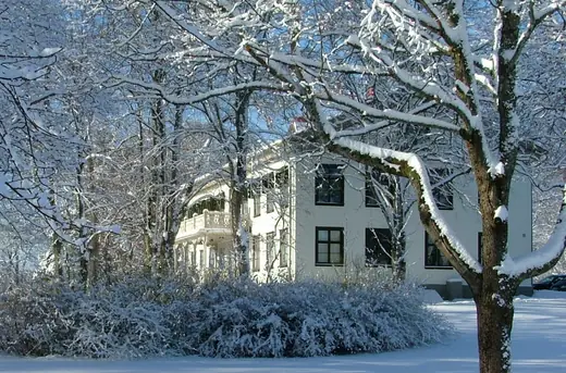 Yellow two-storey manor house with a snow-covered lawn and bare trees.