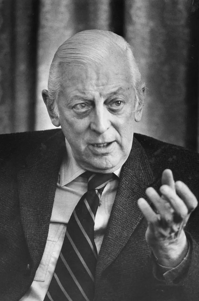 Head-and-shoulders portrait of a man in a suit and tie mid-sentence during an interview, gesturing with his left hand.