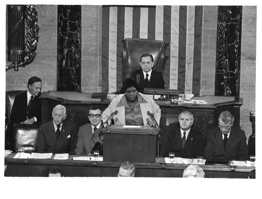 Three people seated together at a formal commemoration in 1974, two of them members of Congress.