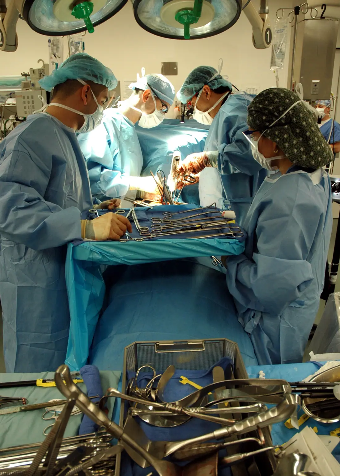 An operating team gathered around a draped table in a hospital theatre, instruments laid out on a tray in the foreground.