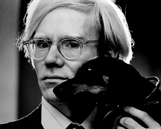 Andy Warhol holding his dachshund Archie against his chest.