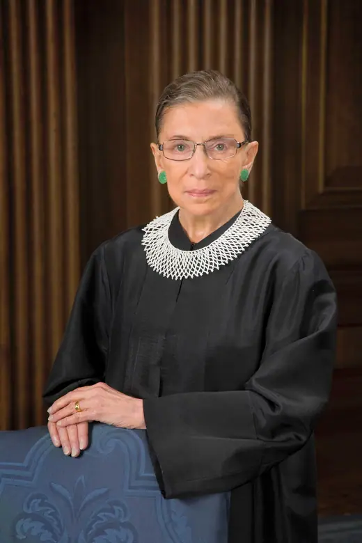 Official robed portrait of Justice Ruth Bader Ginsburg seated before a red curtain.