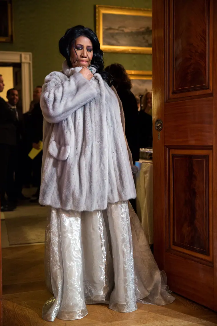 Aretha Franklin in a mink coat, standing in the doorway between the Green Room and the East Room of the White House, April 2015.