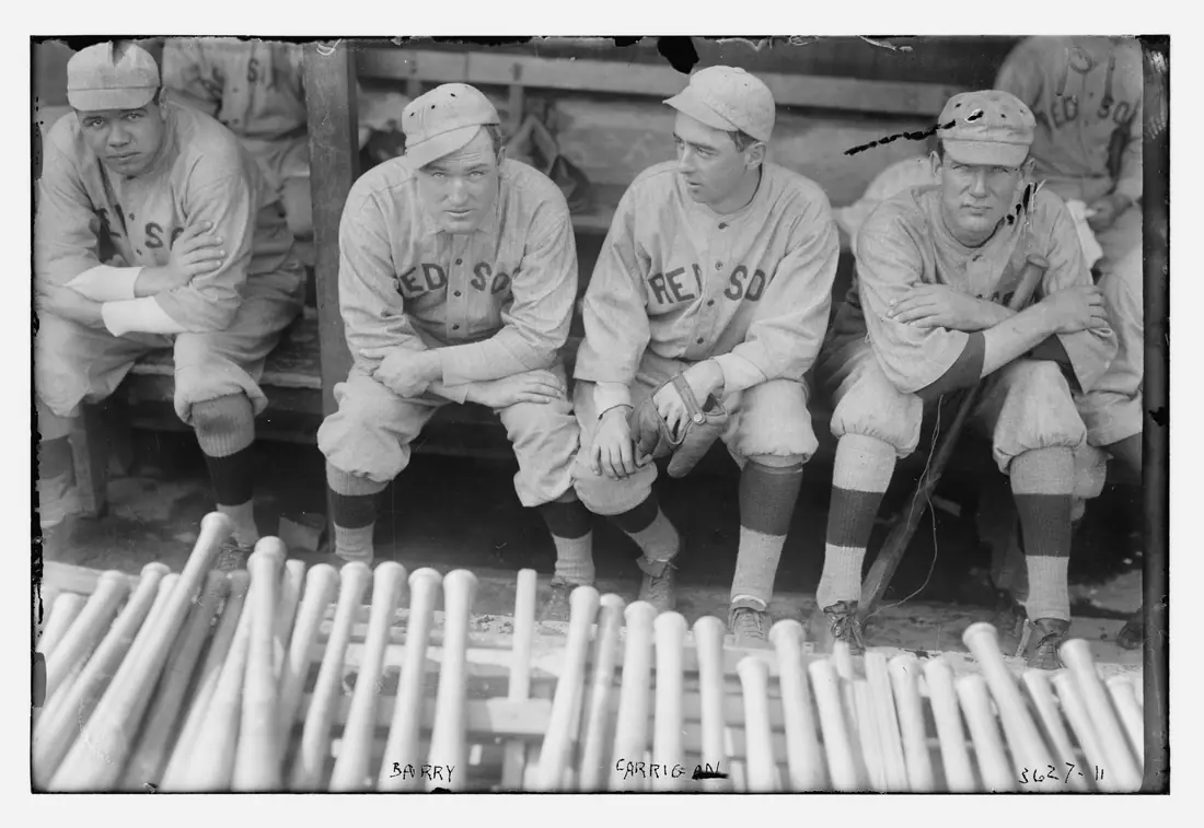 Four baseball players in wool uniforms standing side by side on a field before a game.