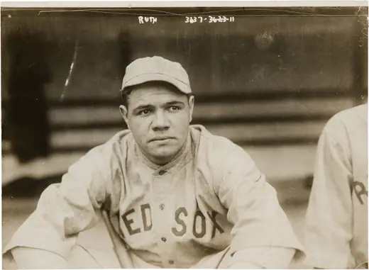 Young ballplayer in a dark uniform, photographed close up in a stadium.