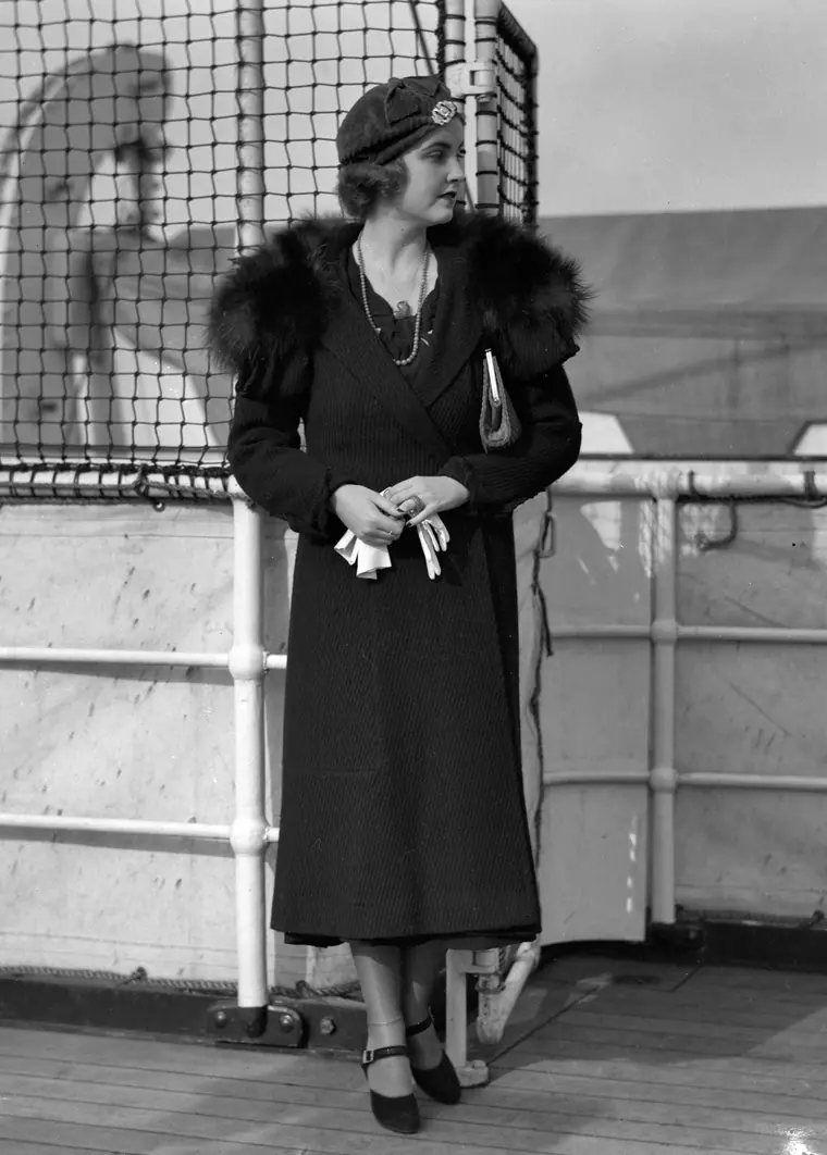 Barbara Hutton standing on a ship's deck in fur, holding a pair of white gloves.