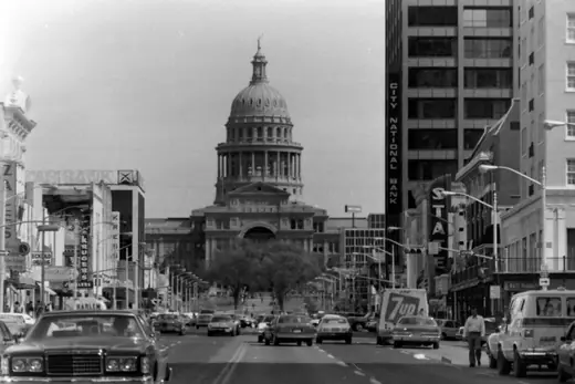A wide avenue of low commercial buildings leading toward a domed capitol in the distance.