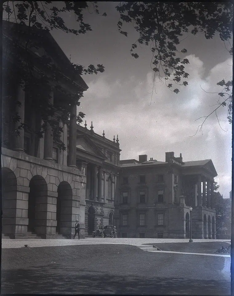 Neoclassical stone courthouse with a columned portico behind iron railings, bare trees in front.