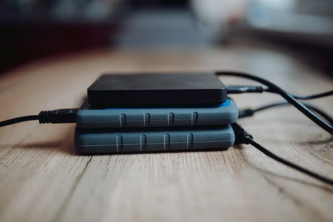 Three portable external hard drives stacked on a wooden table.