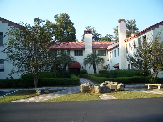 A long two-storey Mediterranean-style lodge with arched windows under live oaks.