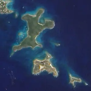Satellite image of the eastern end of St. Thomas and the small islands off its coast, ringed by pale reef water.