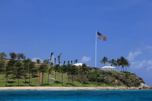A small green island with low buildings seen across open water from a boat.