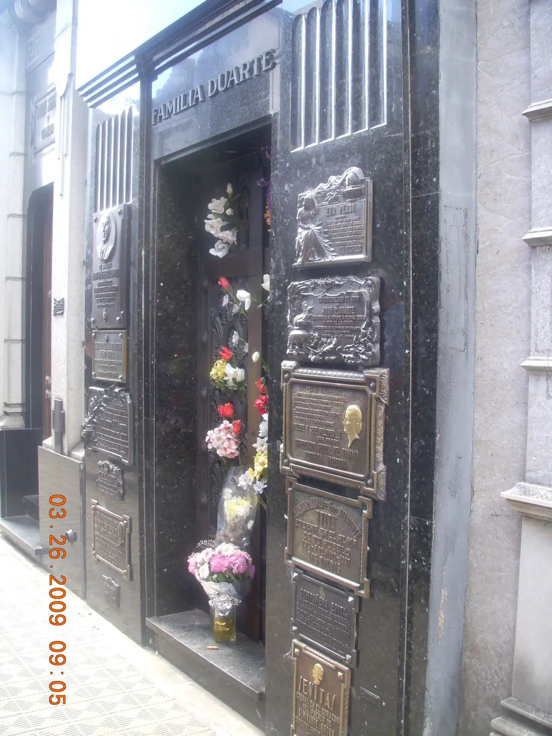 The Duarte family vault at Recoleta Cemetery in Buenos Aires, a black stone tomb covered in memorial plaques and flowers.