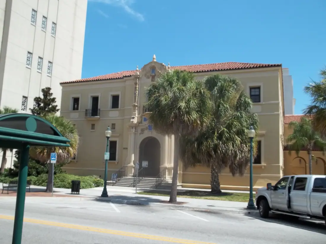 The long arcaded facade of the 1927 Sarasota County Courthouse behind palms and a lawn.