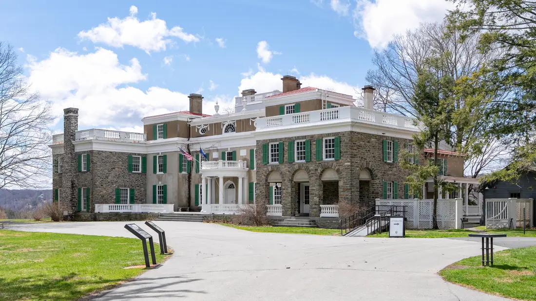 Wide photograph of Springwood, a large stucco and fieldstone house with a columned portico and flanking wings, seen across a lawn.