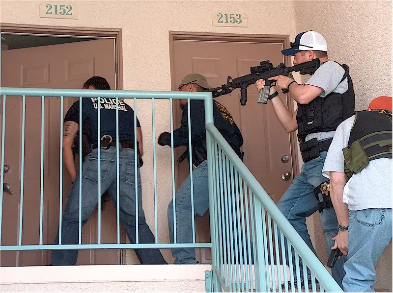 Federal officers in tactical vests at the door of a residence during a multi-agency operation.