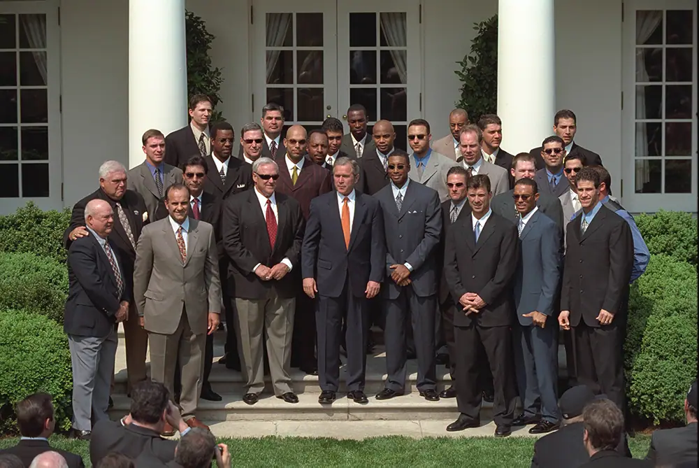 Large group of men in suits and baseball uniforms arranged on steps in a garden with a president at the centre.