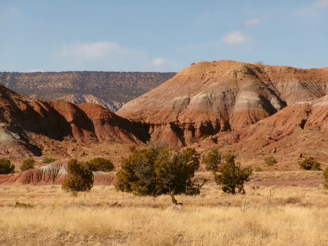 Wide view of red and ochre sandstone cliffs rising above scrub desert at Ghost Ranch, New Mexico.
