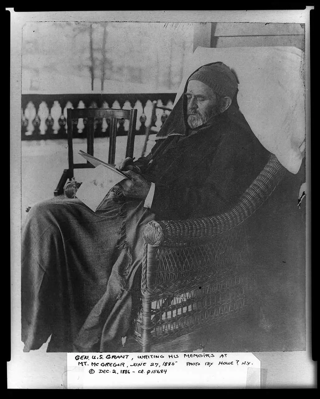 Photographic print of General Grant writing on the porch of the Mount McGregor cottage, surrounded by papers.