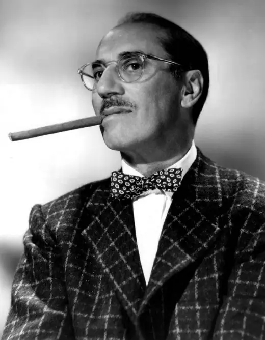 Comedian leaning forward with a cigar, eyebrows raised, network publicity photograph.