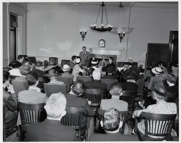 A 1950 photograph of a class in archives administration and genealogical research seated at long tables in a records room.