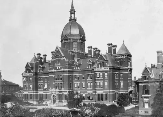 Early photograph of the Johns Hopkins Hospital complex seen across open ground, with its central dome and long brick pavilions.