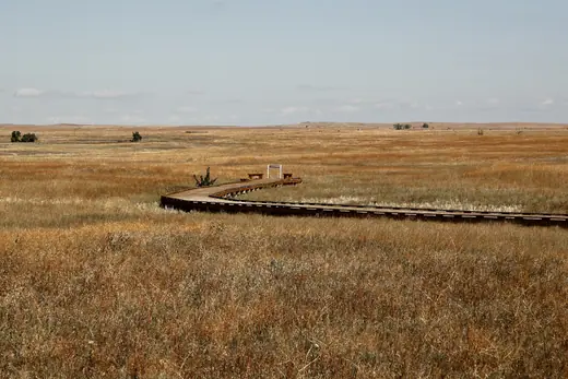A boardwalk running out through open prairie grass toward a low horizon in the South Dakota Badlands.
