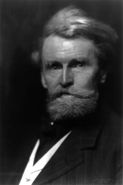 Studio photograph of an elderly man with a full white beard in a dark suit, seated and facing forward.