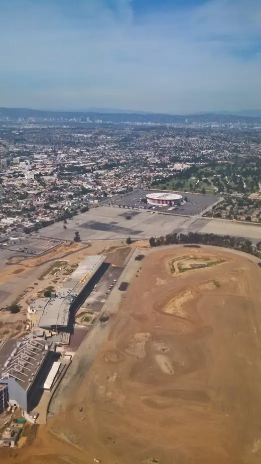 Aerial view of a circular colonnaded arena beside a parking lot.