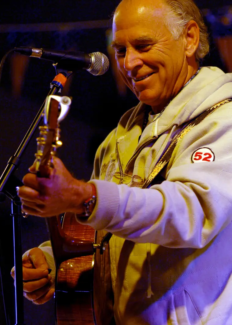 Man in a short-sleeved shirt playing an acoustic guitar and singing into a microphone on a ship's hangar deck.