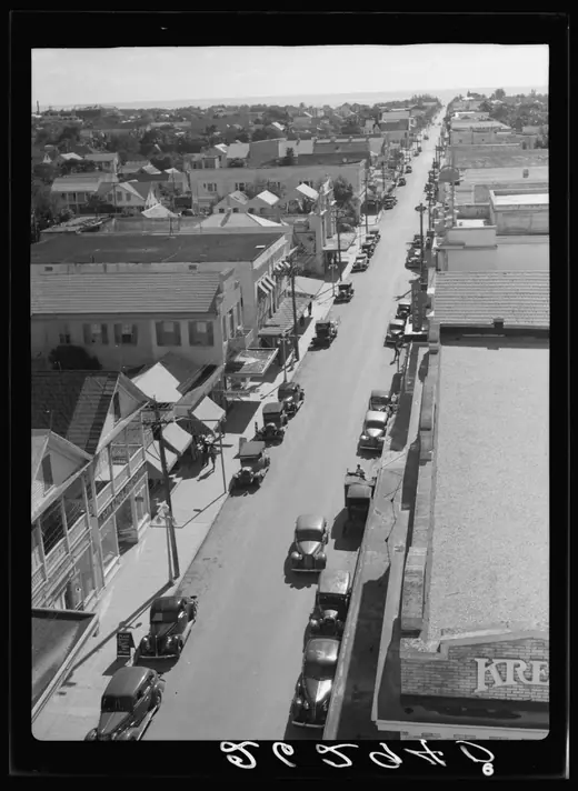 Black-and-white view down a narrow Key West street of low wooden storefronts and awnings.