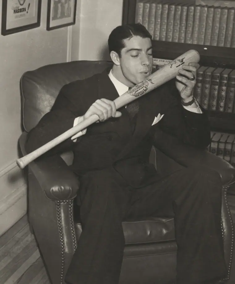 Black-and-white studio portrait of a ballplayer in a pinstriped uniform holding a bat upright beside his face.