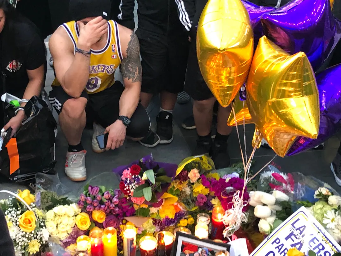 Flowers, jerseys, and handwritten signs piled on a plaza outside a downtown arena.