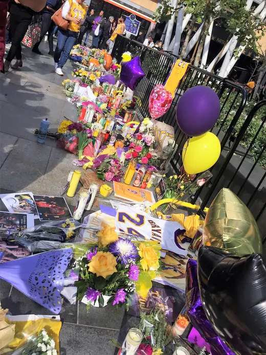 Makeshift memorial of bouquets and candles on a sidewalk outside an arena.