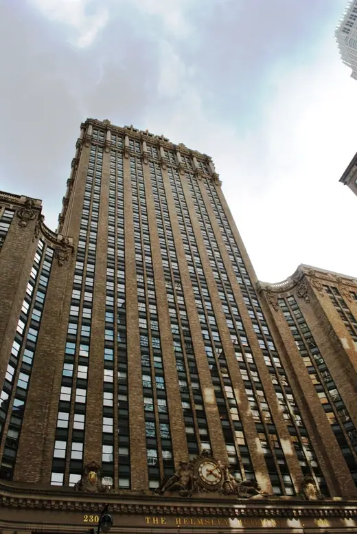 Ornate gilded-crown tower straddling Park Avenue, seen from street level between modern glass buildings.