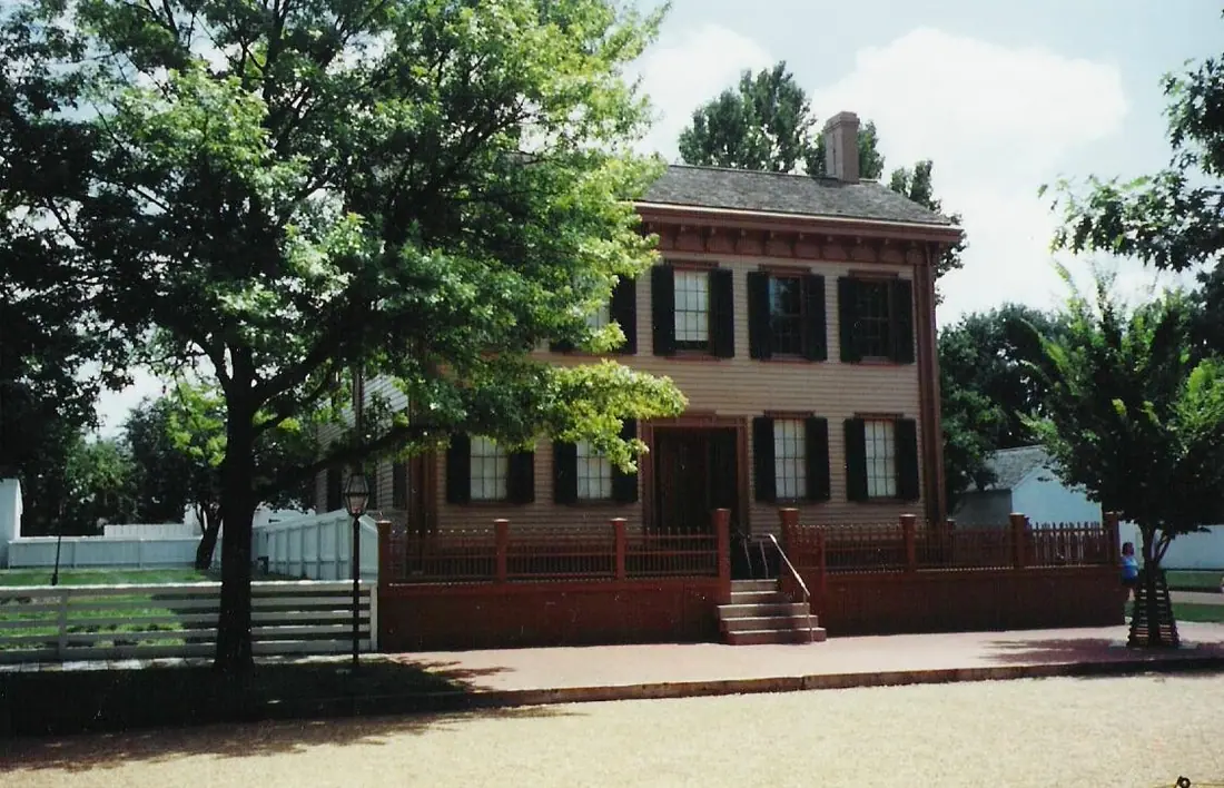 Two-storey clapboard house painted brown with dark green shutters, behind a wooden fence in Springfield, Illinois.