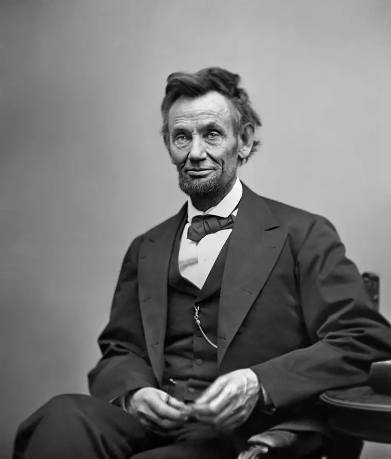 Seated three-quarter-length photograph of Abraham Lincoln holding his spectacles and a pencil.