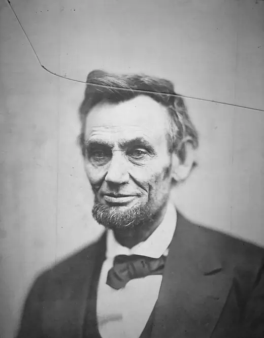 Close portrait of a faintly smiling Abraham Lincoln, with a long crack across the top of the image from the damaged glass negative.