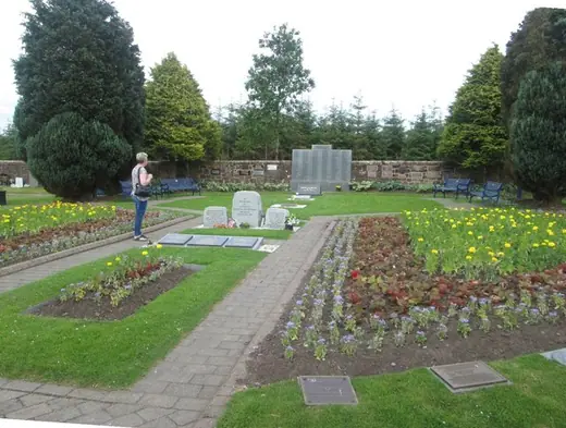 The memorial garden at Lockerbie Cemetery, with low walls and mown grass under a grey sky.