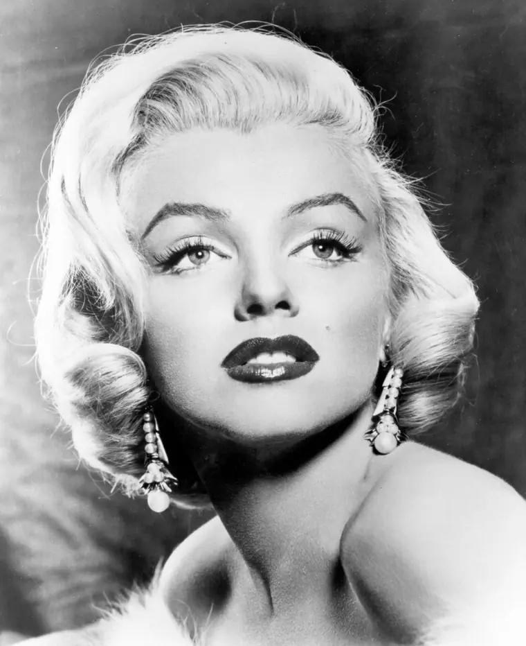 Black-and-white studio publicity portrait of Marilyn Monroe looking over one bare shoulder, hair lit from behind.