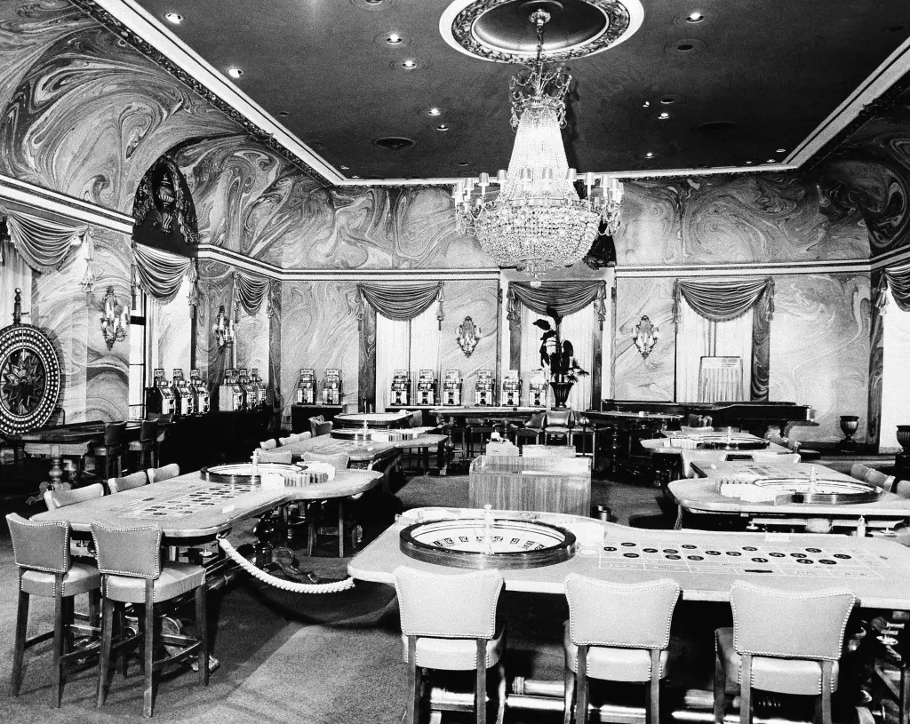 Interior of a 1950s Havana casino, with gaming tables, chandeliers and patrons in evening dress.