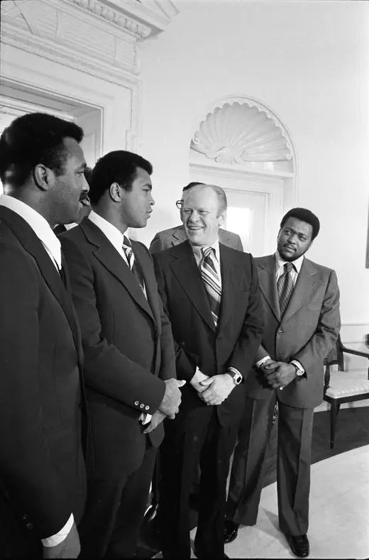 A group of men standing in the Oval Office with the President, one of them a boxer in a light suit.