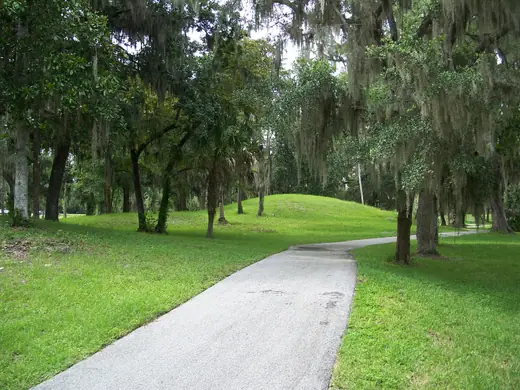 A low earthen mound covered in grass and trees near the plaza at Crystal River Archaeological State Park.