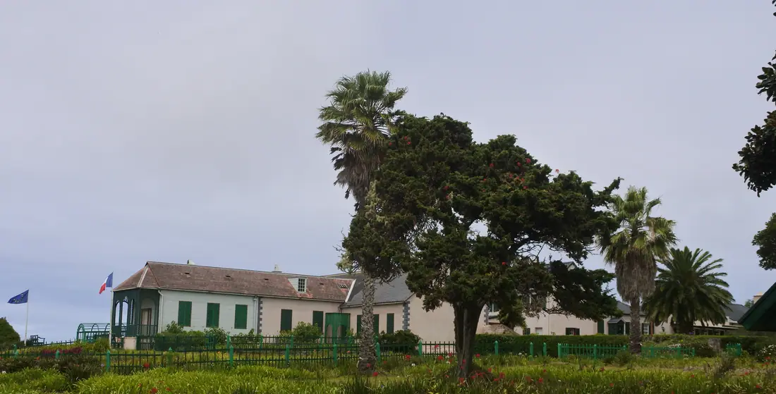 Longwood House on Saint Helena, a long single-storey white building with a green roof, seen across its garden.