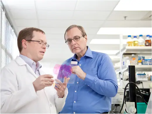 Paul Allen examining a brain sample alongside a scientist in a laboratory.