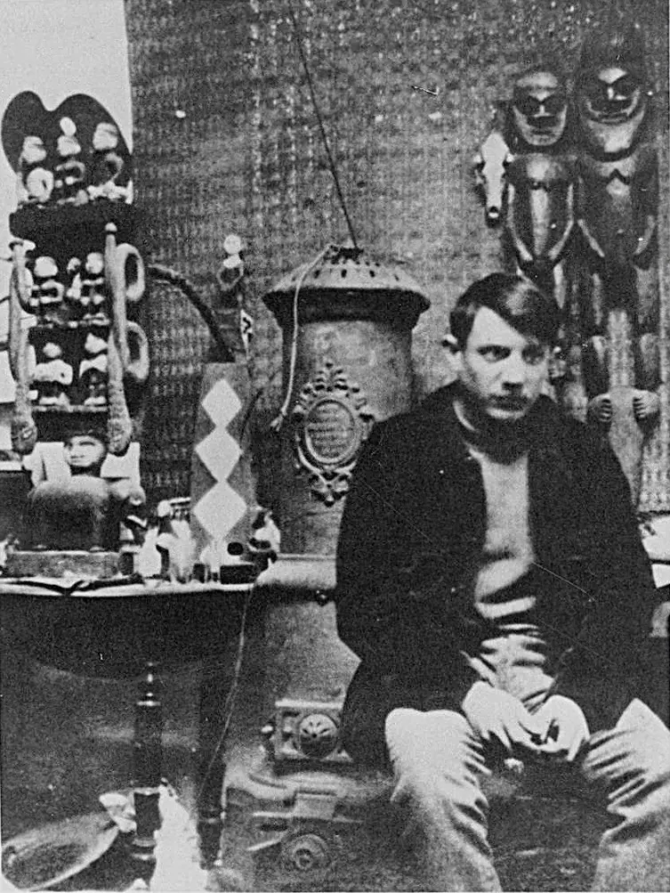 Pablo Picasso seated in his Montmartre studio in 1908, surrounded by canvases and African sculpture.
