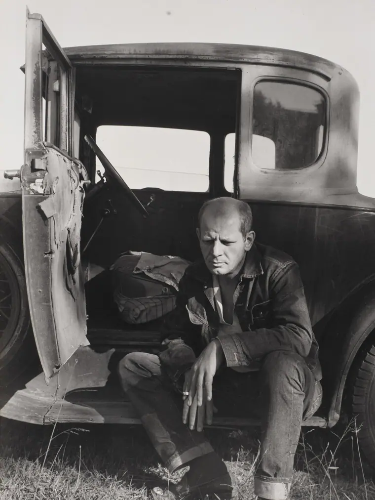 Photographic portrait of Jackson Pollock in a denim jacket, smoking, looking at the camera.